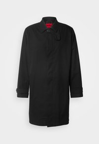 Manteau homme noir longueur genou avec col, bouton supérieur unique et brides de manches boutonnées sur fond uni.