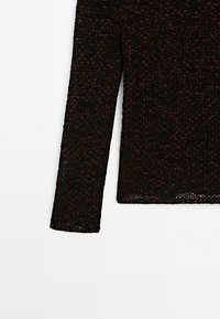 Gros plan d’une manche et du bas du torse d’un pull en maille noir et rouge foncé à manches longues sur fond blanc.