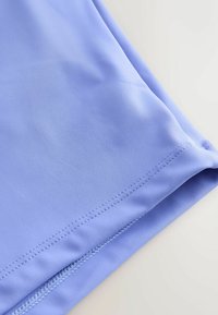 Gros plan sur un tissu bleu clair avec une couture double rangée visible et une texture lisse sur un bord plié.