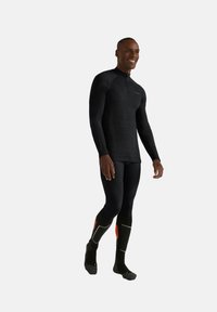 Czarny top z długim rękawem z zamkiem do ćwiartki i teksturowanym wzorem, w połączeniu z czarnymi legginsami oraz czarnymi skarpetkami za kolano z pomarańczowymi akcentami.