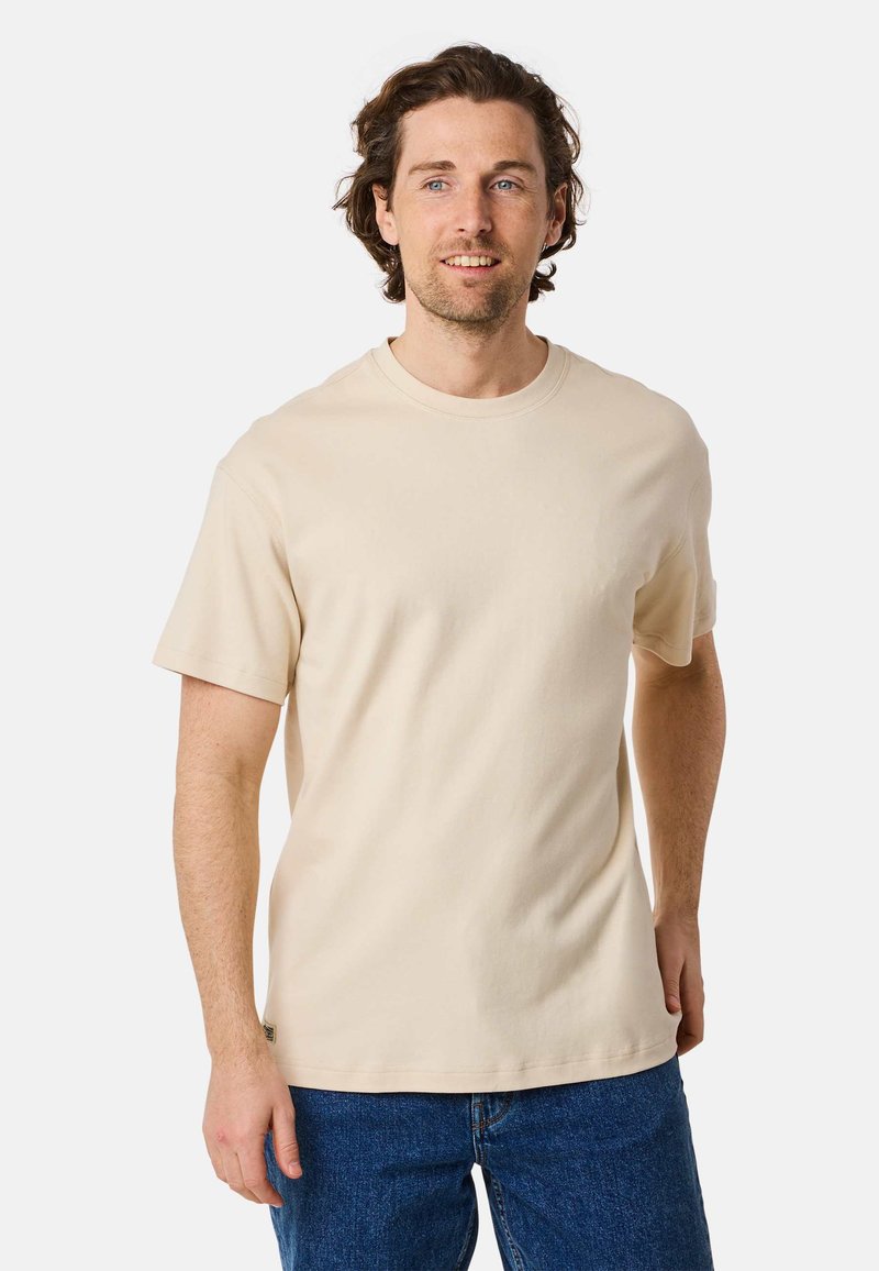 Beige cotton t-shirt with a crew neckline and short sleeves. Smooth texture; fitted silhouette, worn with blue denim jeans.