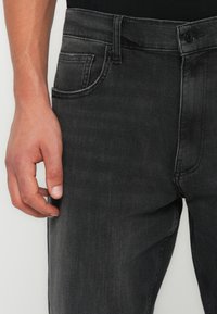 Jeans in denim nero con un classico design a cinque tasche, leggera scoloritura e una chiusura con zip standard accompagnata da un bottone.
