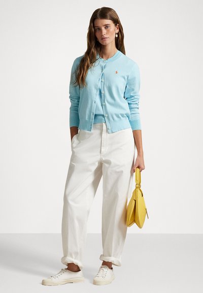 Cardigan azzurro chiaro con chiusura a bottone, indossato sopra un top coordinato. Abbina pantaloni bianchi a vita alta e una borsa gialla. Sneakers casual.