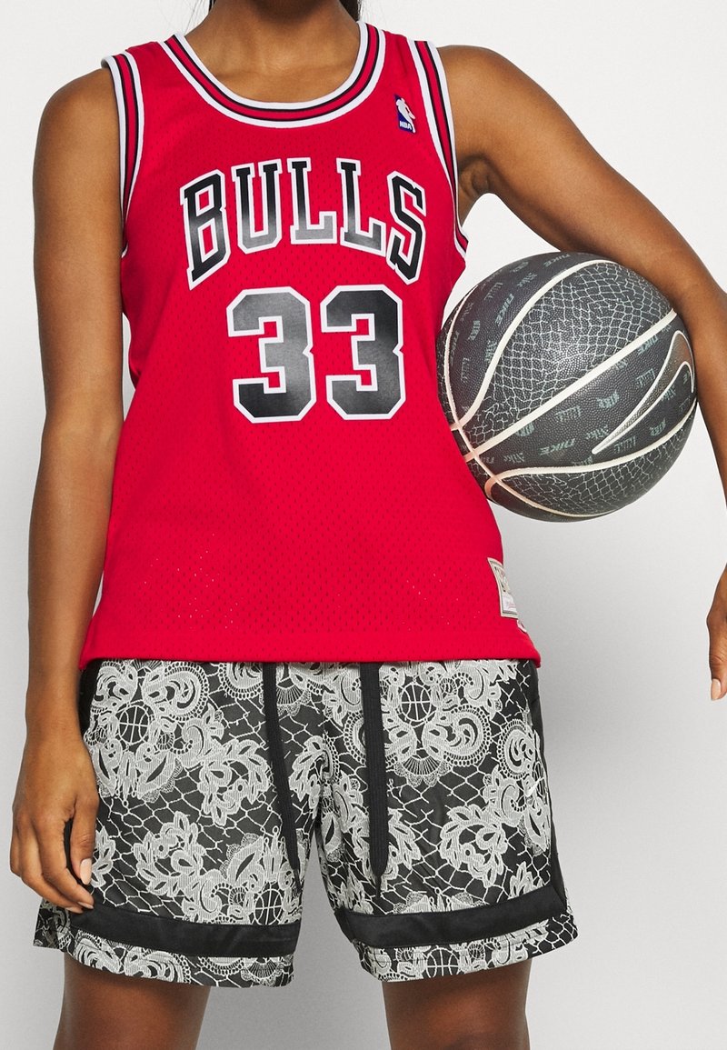 Punainen koripallopaita mustilla yksityiskohdilla ja numerolla 33. Mustat shortsit, joissa on valkoinen pitsikuvio ja musta nyöritys, joka luo kontrastia.