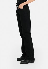Jeans in denim nero con vita alta e taglio dritto. Presentano tasche frontali, dettagli in bottone argentato e una finitura leggermente strutturata.