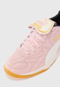 Roosa Puma King sneaker valge riba, kummiselja, paelad ja bränditud klapp keelel valge tausta vastu.