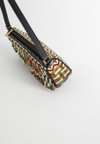 Torebka na ramię z wielokolorowym haftem geometrycznym, koralikowym frędzlem, czarnym paskiem i zamknięciem na zamek błyskawiczny na białym tle.