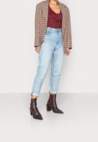 Blazer oversize a quadri marroni, top borgogna con volant, jeans a vita alta azzurri chiari e stivali alla caviglia borgogna con tacco a blocco.