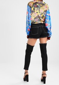 Svarta denimshorts med fransade kanter, matchade med en färgglad blommönstrad långärmad topp med blå ärmar och en oversized design.