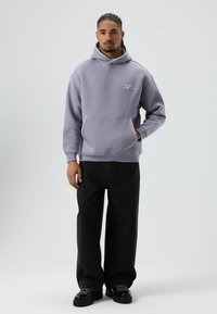 Paarse fleece hoodie met een kangoeroezak, geribbelde manchetten en een capuchon met trekkoord, gecombineerd met zwarte wijde jeans en chunky zwarte schoenen.