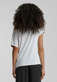 T-shirt blanc, ample, avec un col large et des manches courtes. Texture douce, ourlet arrondi et détails noirs contrastants sur les manches.