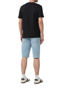 Schwarzes Baumwoll-T-Shirt, kombiniert mit hellblauen Jeansshorts. Weiße und schwarze Sneaker mit grauen Akzenten und sichtbaren weißen Socken.