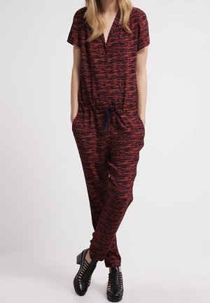 Tuta intera con motivo rosso e nero, maniche corte, scollo a V, vita con coulisse e tasche laterali, abbinata a scarpe nere con cinturini.