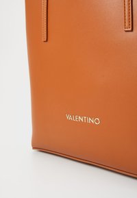 Brun skinnveske med to lange håndtak, med preget "VALENTINO"-logo i gull. Glatt tekstur og minimalistisk design.