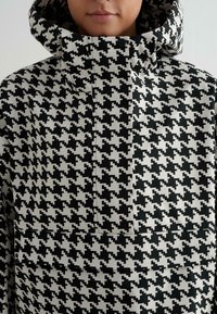 Hoody met een groot zwart-wit pixelachtig houndstooth patroon, voorflap en drukknoopsluiting bij de hals.
