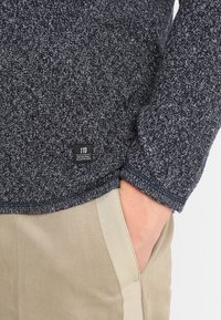 Chemise à manches longues bleu marine texturée avec un motif tissé et une petite étiquette noire affichant "TTD ORIGINAL CLOTHING" près de l'ourlet.