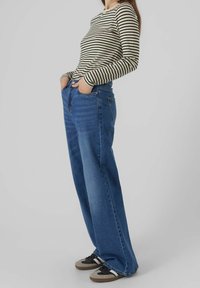 Camisa de rayas de manga larga combinada con unos vaqueros azules de corte holgado. Los vaqueros tienen una cintura de altura media, bolsillos frontales y una textura clásica de denim.