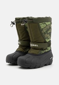Botas aislantes verdes y negras con un diseño de camuflaje, suelas de goma, cordón ajustable y tira de Velcro etiquetada "SOREL."