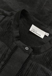 Blouse noire à texture plissée, col rond et fermeture par boutons. Étiquette indiquant "KAREN BY SIMONSEN", taille EU 38 / US 8.