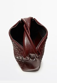 Borsa di pelle color bordeaux con texture intrecciata e dettagli lisci, dotata di chiusura superiore con cerniera e singolo cinturino a tracolla.