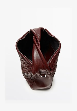 Bordowa skórzana torba o plecionej fakturze z gładkimi akcentami, wyposażona w zamknięcie na suwak od góry oraz pojedynczy pasek na ramię.