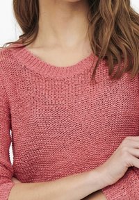 Sweter na drutach w jasnoróżowym kolorze, z szerokim dekoltem i teksturowanym wzorem, z rękawami o długości do łokcia.