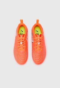 Zapatillas deportivas de color naranja brillante con superficie texturizada, que presentan patrones de puntos blancos, cordones y una lengüeta para tirar en el talón. Plantilla de color amarillo neón.