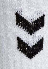 Calcetín blanco de punto con dos patrones de chevrón negros, dispuestos verticalmente. La textura parece suave con una costura uniforme en todo el calcetín.