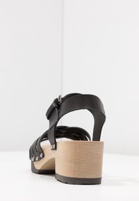 Zwarte leren sandalen met hak en een houten plateauzool, voorzien van een riemontwerp met metalen hardware en een gladde textuur.