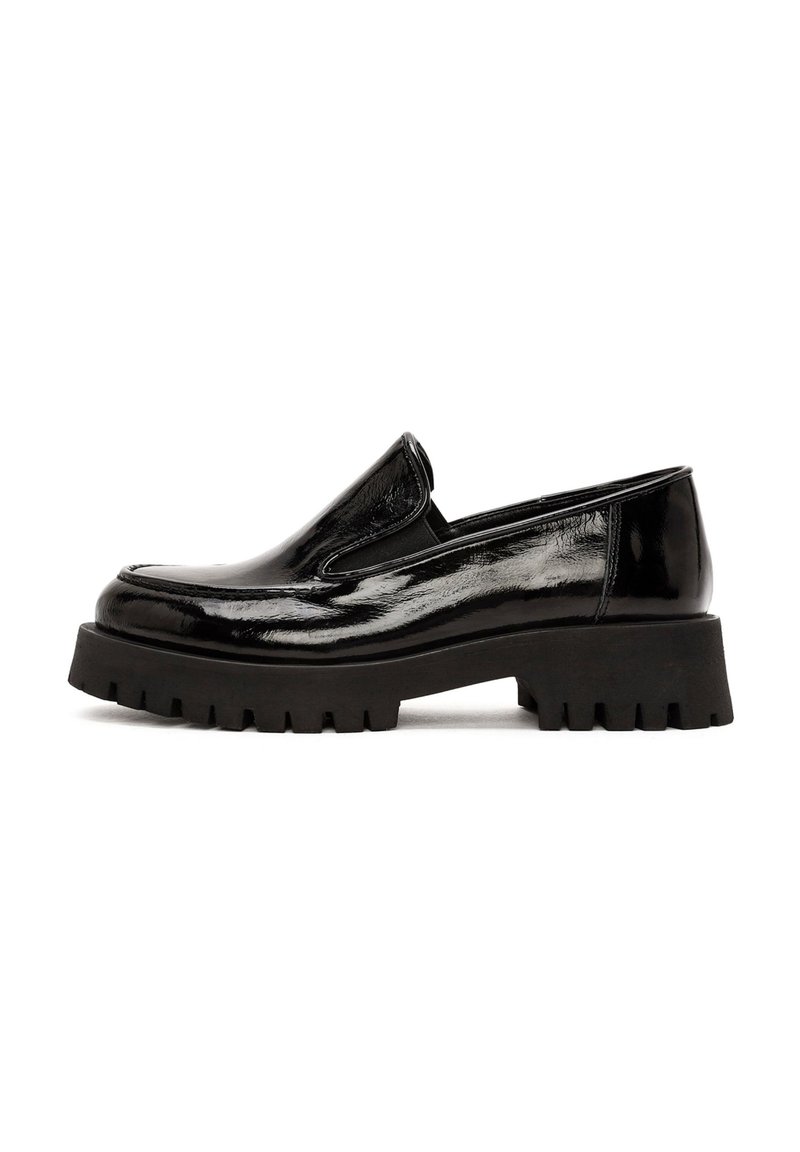Scarpa slip-on in vernice nera con suola in gomma spessa e presa testurizzata. Presenta una punta arrotondata e dettagli elastici laterali.