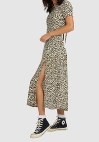 Kwiatowa sukienka midi z krótkim rękawem, czarne tło, wzór w żółte i białe kwiaty, rozporek po boku; w zestawie z czarnymi trampkami za kostkę.