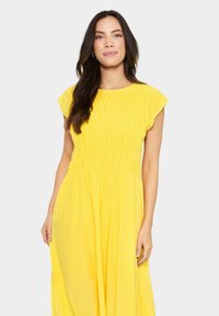 Yellow dress with a smocked bodice, short sleeves, and flowing skirt. Made from lightweight fabric, features a soft texture and bright color.