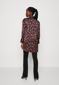 Lepardo rašto marškiniai-jaketa juodos ir rusvos spalvų, ilgomis rankovėmis, su apykakle ir ilgesniu nugara, užsimauti virš juodų kelnių.