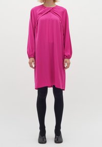 Fuksia pitkähihaine mekko, jossa on kerätty pääntie, väljä malli ja hieman teksturoitu kangas; päällä mustat legginsit ja korot.