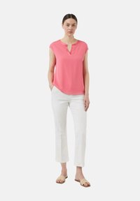 Rosa Bluse mit kurzen Ärmeln und V-Ausschnitt, kombiniert mit weißen, geraden Hosen und hellen Sandalen. Einfaches, entspanntes Design.