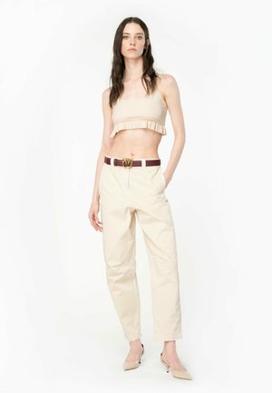 Top corto a coste beige con orlo a balze, abbinato a pantaloni cream a sigaretta, fissato con una cintura bordeaux con fibbia dorata.