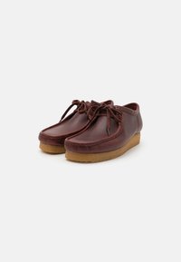 Chaussures en cuir marron avec un bout rond, un laçage et une semelle beige rembourrée, présentant des coutures soignées le long des bords.