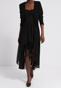 Černé šaty s přiléhavým korzetem, nařasenými detaily a mnohovrstvým asymetrickým lemem. Kombinované s krátkým černým sakem a černými podpatky.