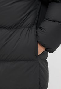 Black puffer jacket featuring a quilted design, side pockets, and a smooth, shiny texture. Shell and lining are made from synthetic materials.