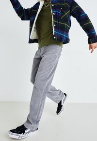Chaqueta de franela a cuadros con forro de borreguillo, sudadera verde oliva, pantalones de pana grises y zapatillas negras con acentos de llamas.