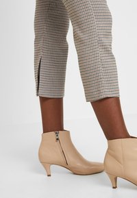 Beige läderankelboots med spetsig tå och liten klack, med sidodragkedja och slät yta, kombinerade med mönstrade byxor.