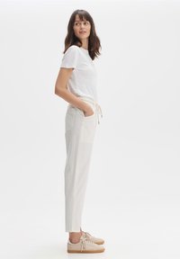 Witte T-shirt met korte mouwen, gecombineerd met lichtbeige sweatpants met touwtje. De outfit bevat lichtgekleurde sneakers.