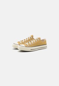 Gule lerrets sneakers med hvite snørebånd, gummitåhette og svart stripe detalj langs sålen. Lav toppdesign og teksturert stoff.