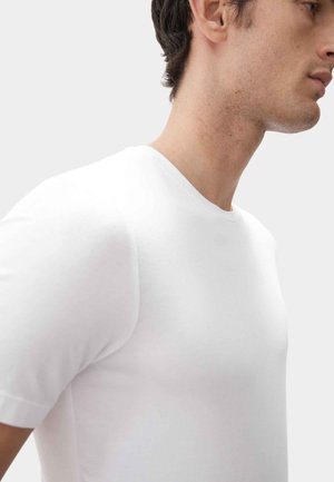 Camiseta blanca de manga corta, hecha de una tela suave y lisa, con un clásico cuello redondo y silueta ajustada, presentada sobre un fondo neutro.