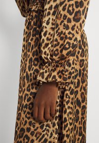 Klänning med leopardmönster som har ett brunt och svart mönster, lättviktsmaterial, samlade elastiska manschetter och en avslappnad passform med en flödande silhuett.