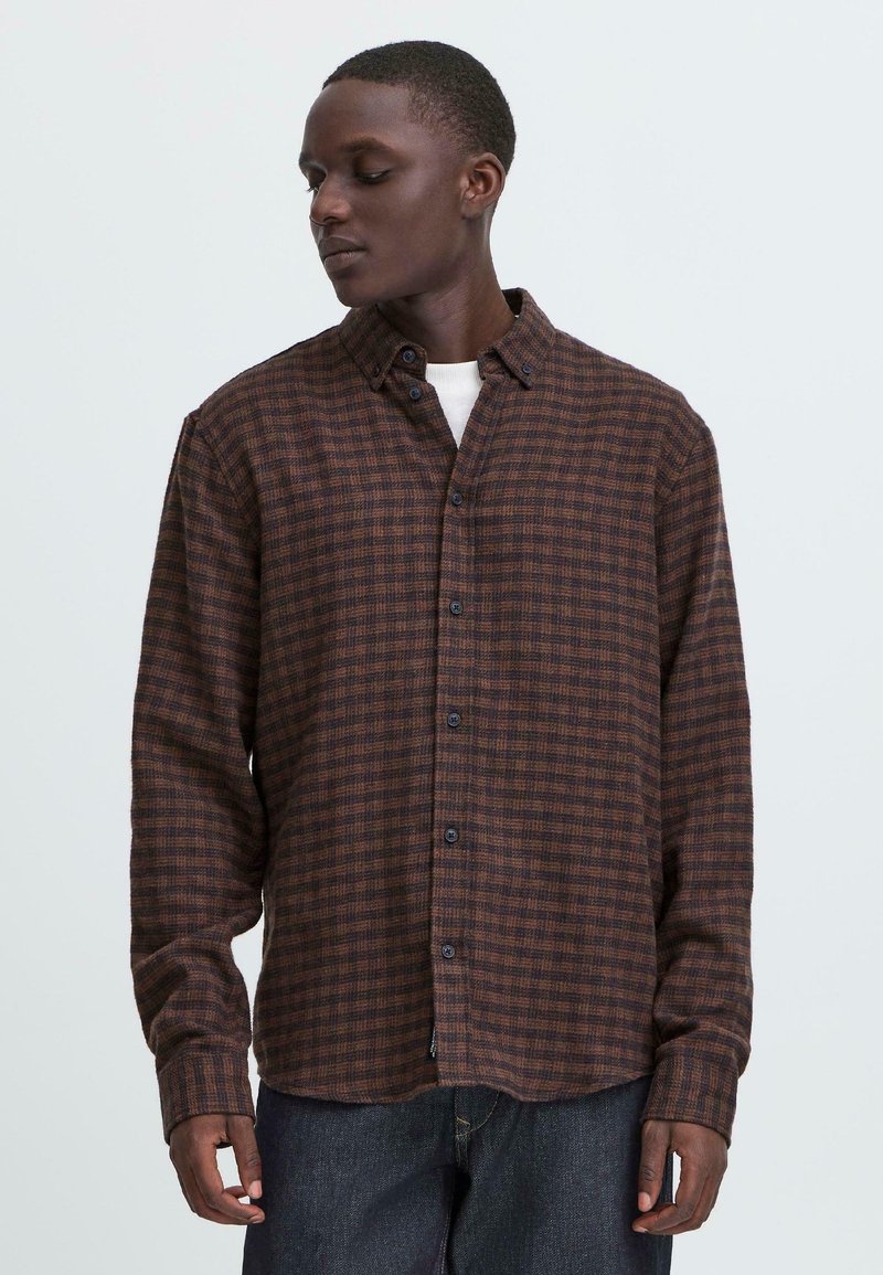 Camisa de cuadros marrones de botones con mangas largas, con botones azules y un dobladillo ligeramente curvado, hecha de una tela texturizada.