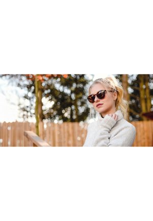 Tortoiseshell cat-eye sunglasses with dark lenses, complemented by a light gray knitted sweater. Soft outdoor lighting enhances the scene.