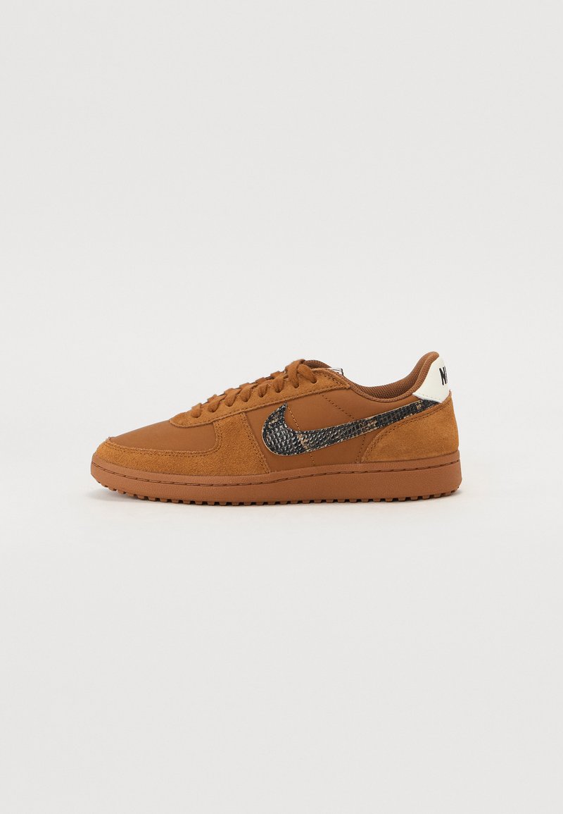 Sapatilhas de camurça e couro castanho com o swoosh preto da Nike, detalhes texturizados, bico redondo e sola de borracha plana. A parte traseira apresenta a marcação da Nike em branco.