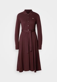 Rochie lungă de culoare vișinie, dintr-un material moale, cu guler, fermoar în față, mâneci lungi și o curea legată în talie. Detaliu cu logo-ul Lacoste.