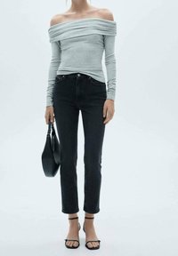 Top gris claro sin mangas con largas mangas, combinado con jeans negros de tiro alto. Tacones negros con tiras y un bolso negro pequeño.